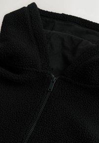 Schwarzer Fleece-Hoodie mit strukturiertem Äußeren, Reißverschluss und weicher Innenauskleidung. Verfügt über eine Kapuze und keine sichtbaren Muster oder Akzente.