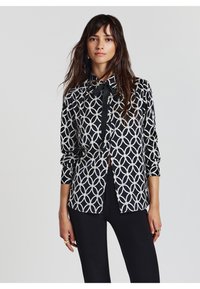 Schwarzes und weißes Musterhemd mit geometrischem Design, Kragen und durchgehender Knopfleiste. Lange Ärmel mit geknöpften Manschetten.