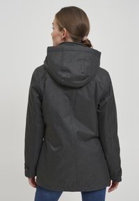 Mørk grå hettegenser med teksturert stoff. Har innsnevret liv, mansjettknapper og et enkelt, rent design.