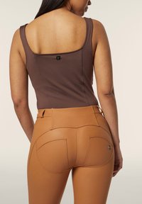 Ruskea slim fit -toppi, jossa on logo takana, yhdistettynä korkeavyötäröisiin, vaaleanruskeisiin legginsseihin, joissa on kaksi takataskua ja yksityiskohtainen ompelu.