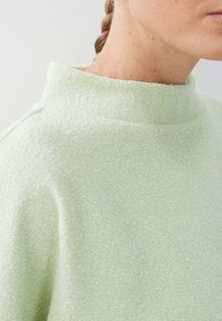 Tessuto verde chiaro con texture, dotato di un alto colletto e una sensazione morbida e pelosa. La prospettiva ravvicinata enfatizza l'aspetto del materiale.