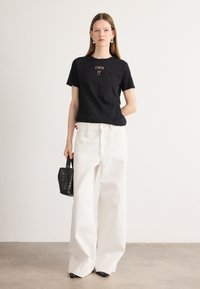 Svart bomulls t-skjorte med "OWN IT" tekst i gull. Kombinert med brede hvite jeans og en liten svart flettet håndveske. Svart spissesko.