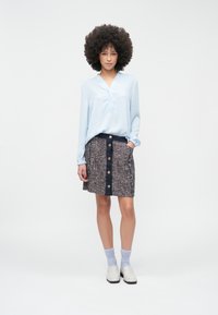 Hele sinine pikkade varrukatega pluus ja tekstuurse mustriga seelik tumesinise vöökohaga ning nööpidega, kombineeritud hallide sokkide ja valgete kingadega.