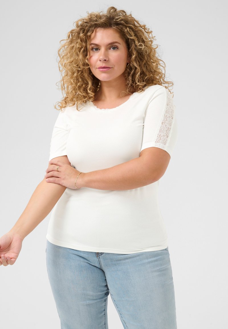 T-shirt blanc à côtes avec des manches courtes, présentant des accents en dentelle sur les épaules. Texture douce, design ajusté, col rond et léger stretch.