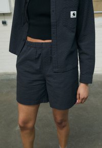 Donkergrijze shirt en shorts set in een gestructureerde stof. Het shirt heeft een zak en een klein logo patch. Elastische tailleband op de shorts.