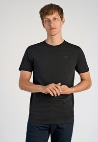 Musta puuvillapaita lyhyillä hihoilla, pyöreällä kauluksella ja huomaamattomalla logolla rinnassa. Sileä pinta ja normaali istuvuus.