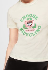 Béžové tričko se zeleným nápisem „Choose Recycling“ kolem růžové řečnické bubliny s okem a zeleným symbolem recyklace.