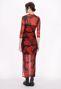 Durchsichtiges schwarzes langärmliges Kleid mit rotem Rosenmuster, figurbetontes Design, gespaltene Rockpartie, kombiniert mit schwarzen Knöchelstiefeln.