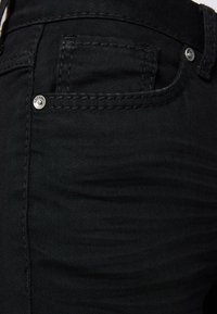 Jeans de mezclilla negra con una textura suave, que cuentan con un pequeño bolsillo frontal, detalles de remaches plateados y costuras en tono a lo largo de las costuras.