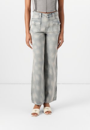 Wide-leg jeans in light blue denim with faded patches, featuring front pockets and a high waist, paired with cream open-toe slides.