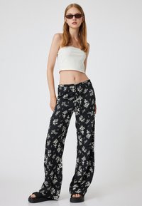 Svarta blommönstrade byxor med vida ben och dragsko i midjan, kombinerat med en vit ribbad crop top och svarta plattformssandaletter.