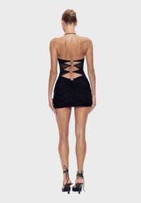 Zwarte mini-jurk met een gerimpelde textuur, strapless ontwerp en een uitgesneden rug met metallic hardware accenten. Gecombineerd met gespsandalen.