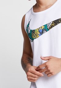 Camiseta sin mangas blanca con un logotipo de Nike de colores múltiples, que presenta formas abstractas y acentos de tablero de ajedrez en la zona del pecho.