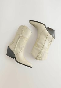 Vita läder cowboystövlar med spetsiga tår, låg klack och dekorativ sömnad. Har metalldetaljer längs sömmarna och en sidoglidare.