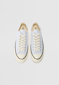 Baskets en toile bleu clair avec des lacets crème, un embout en caoutchouc et un accent noir le long de la semelle. Design plat avec œillets métalliques.