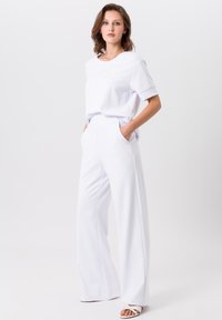 Weißes Baumwollmischoberteil mit kurzen Ärmeln, kombiniert mit hochtaillierten weißen weit geschnittenen Hosen mit seitlichen Taschen und einer glatten Textur.