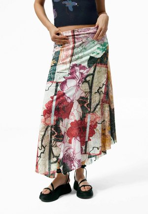 Persona che indossa una gonna asimmetrica con fantasia floreale multicolore, sandali neri con plateau e cinturini, e un top senza maniche in maglia.