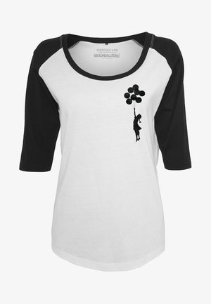 Valge ja must 3/4 varrukatega särk, millel on must siluett graafika kujutis figuurist, kes hoiab õhupalle, pehmest puuvillast tekstuurist.