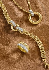 Set di gioielli in tonalità dorata composto da una collana con catena e un ampio pendente circolare, accompagnato da un anello texturizzato con accenti di gemme trasparenti.