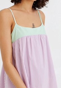 Robe sans manches rayée avec un haut vert clair et un bas lavande. Le tissu est doux, avec une coupe ample et un design de taille froncée.