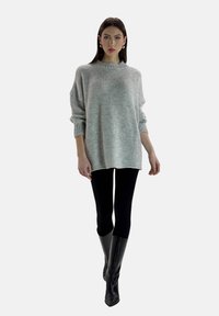Suéter de punto gris claro de gran tamaño con cuello y puños acanalados, combinado con leggings negros y botas negras hasta la rodilla. Tela suave y texturizada.