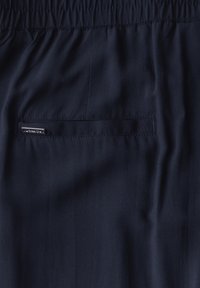 Navyblauwe stof met een gladde textuur, met een elastische tailleband en een klein, rechthoekig achterzakje met een metalen accent.