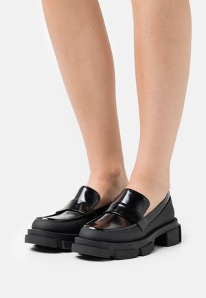 Černé polobotky s lesklým povrchem, s robustní podrážkou a širokým páskem přes přední část. Design je moderní s texturovanými akcenty.