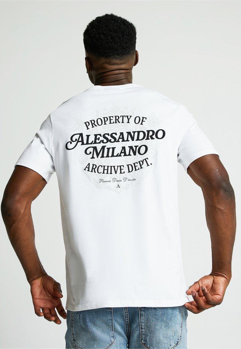 Valkoinen puuvillapaita, jossa on musta graafinen teksti "OMAISUUS ALESSANDRO MILANO ARKISTO-osastolle" ja koristeellinen muotoilu selässä.