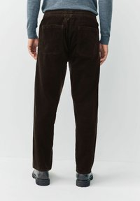 Rear view of person wearing dark brown corduroy pants, gray long-sleeve top, and black boots on plain light background.