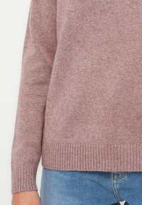 Lys rosa genser med ribbestrikket kant og ermer, laget av et teksturert strikkemateriale, kombinert med lyseblå denimjeans.
