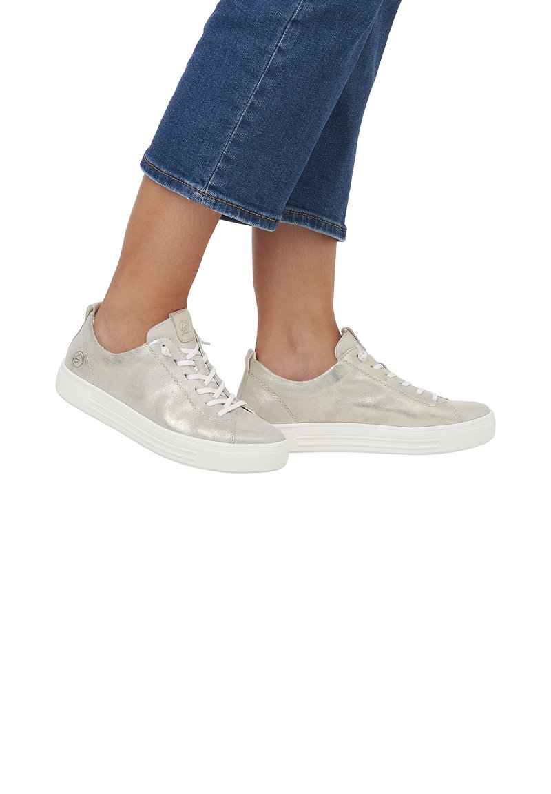 Sneaker metallic silver con design stringato, suole bianche, texture liscia e dettaglio del marchio vicino al tallone. Indossati con pantaloni in denim accorciati.