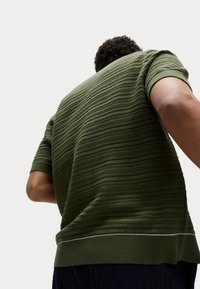 Suéter de punto verde de manga corta con rayas horizontales texturizadas, un cuello redondo acanalado y un detalle blanco en el dobladillo.