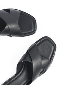 Melnas ādas čības ar kvadrātu formas purngalu. Augšdaļa ir veidota ar divām krustveidīgām siksnām, ar gludu faktūru un minimālām šuvju detaļām.