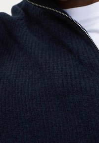 Granatowy sweter z zamkiem błyskawicznym, wykonany na dzianinie, z teksturowaną powierzchnią i srebrnym detalem zamka przy kołnierzu. Miękka tkanina o luźnym kroju.