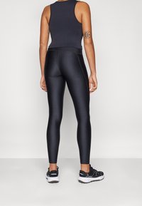 Leggings atletici neri con una texture liscia e scivolosa, abbinati a una canotta scura. L'outfit è completato da scarpe da ginnastica nere.