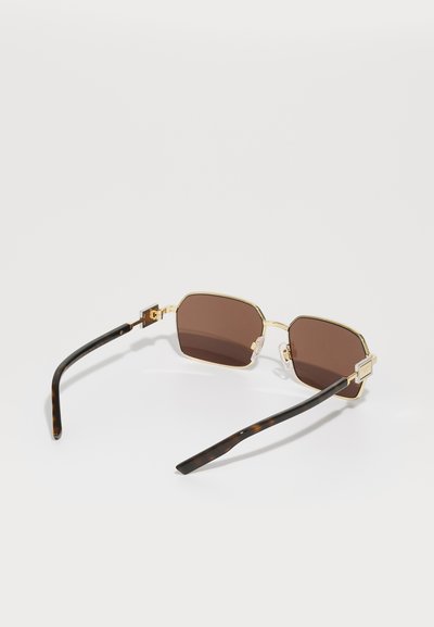 Gold-framed sunglasses with octagonal brown lenses. Tortoiseshell-patterned temple arms. Hinged design, sleek and modern aesthetics.