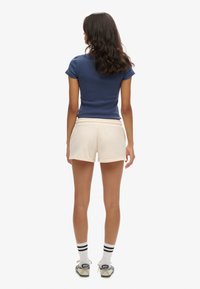 Haut à manches courtes en maille navy, shorts crème avec taille élastique, associé à des chaussettes rayées et des chaussures décontractées.