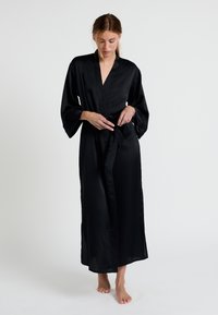 Robe en satin noir de style kimono avec des manches longues, une taille à nouer et une conception fluide pleine longueur. Texture lisse et style minimaliste.
