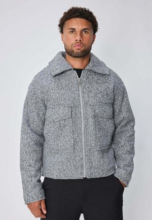 Veste matelassée grise en mélange de laine texturée. Elle présente une fermeture éclair à l'avant, de grandes poches plaquées et un large col. Coupe ajustée, aspect chaud.