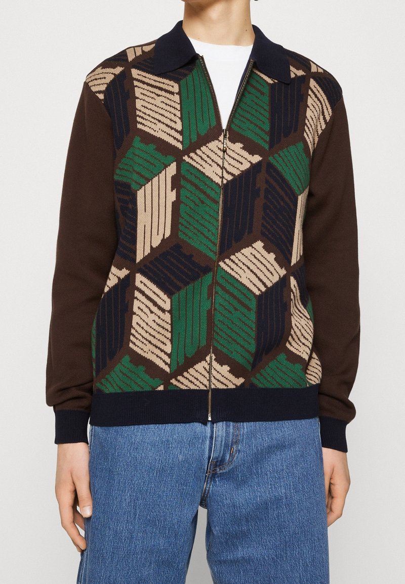 Stickad jacka med dragkedja i brunt med ett geometriskt mönster i grönt, beige och marinblått. Har en ribbad krage och muddar.