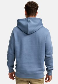 Lyseblå hettegenser laget av mykt stoff med stor hette, ribbede mansjetter og kant, med jevn tekstur og minimalistisk design.