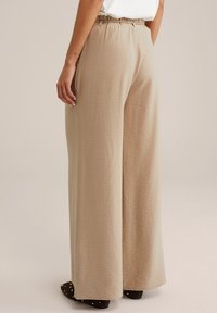 Beige široké kalhoty z texturované látky, s elastickým pasem a volným střihem, doplněné tmavými nazouvacími botami.