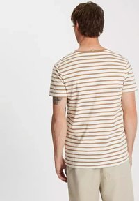 Pasiasta koszulka z beżowymi i białymi poziomymi paskami, krótkimi rękawami, okrągłym dekoltem i luźnym krojem. Lekka tekstura materiału.