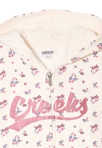 Sudadera con cremallera color crema claro con un patrón floral, texto en purpurina rosa "Creeks" y un forro interior suave.