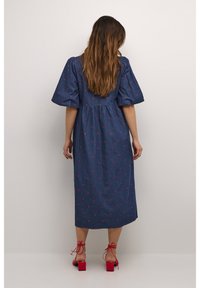 Denim-mittimekko puff-hihnoilla, jossa on vaaleanpunaiset sydänkirjonnat. Yhdistetty punaisiin lohko-korkokenkiin. Takaa nähtynä vyötäröllä on laskostettu malli.