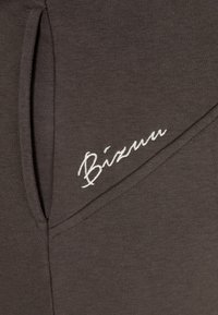 Donkergrijze sweatpants met een soepele textuur, voorzien van een witte geborduurde "Bizuu" logo aan de zijkant en een schuine heupzak.