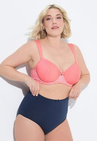 Soutien-gorge corail à pois avec bretelles ajustables et accent nœud, associé à une culotte marine à pois taille haute. Tissu lisse et doux.