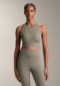 Olivno zelena skrajšana atletska majica z visokim ovratnikom, v kombinaciji z visokim pasom legic. Gladka tekstura in minimalni šivi.