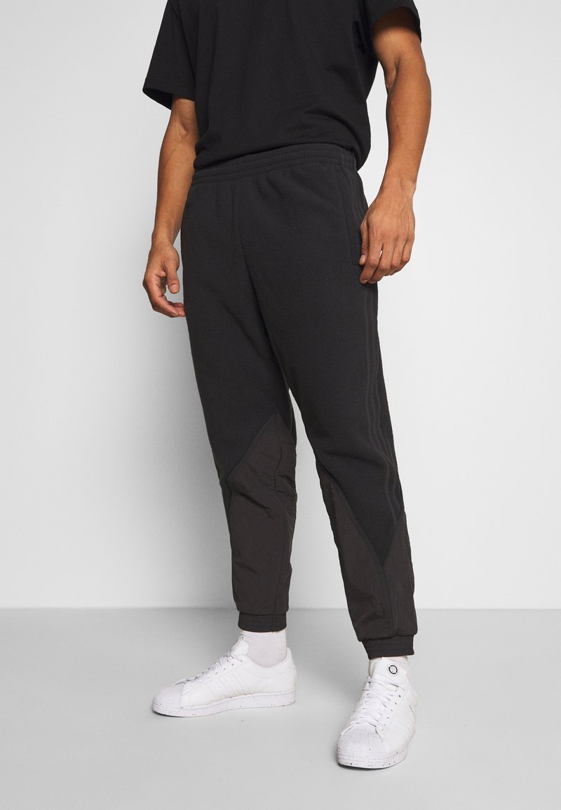 Svarta fleece-joggingbyxor med insvängd passform, elastisk midja, kontrasterande texturerade paneler, tillsammans med vita sneakers och ankellånga strumpor.