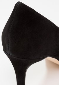 Chaussure à talons hauts en daim noir avec un bout pointu, une silhouette élégante et une texture lisse, dotée d'un talon stiletto slim et effilé.